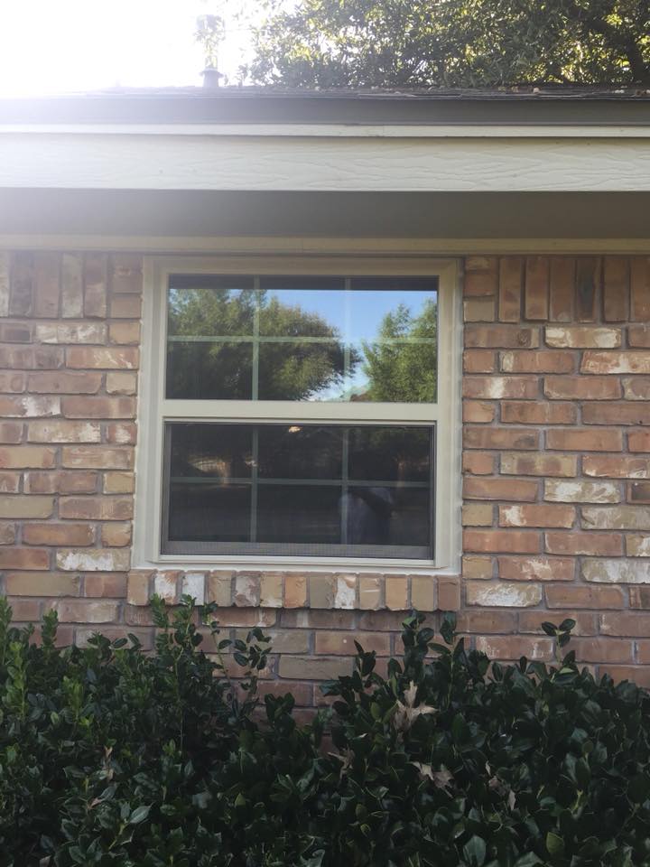 A light-colored window frame and divided glass set into an existing brick exterior